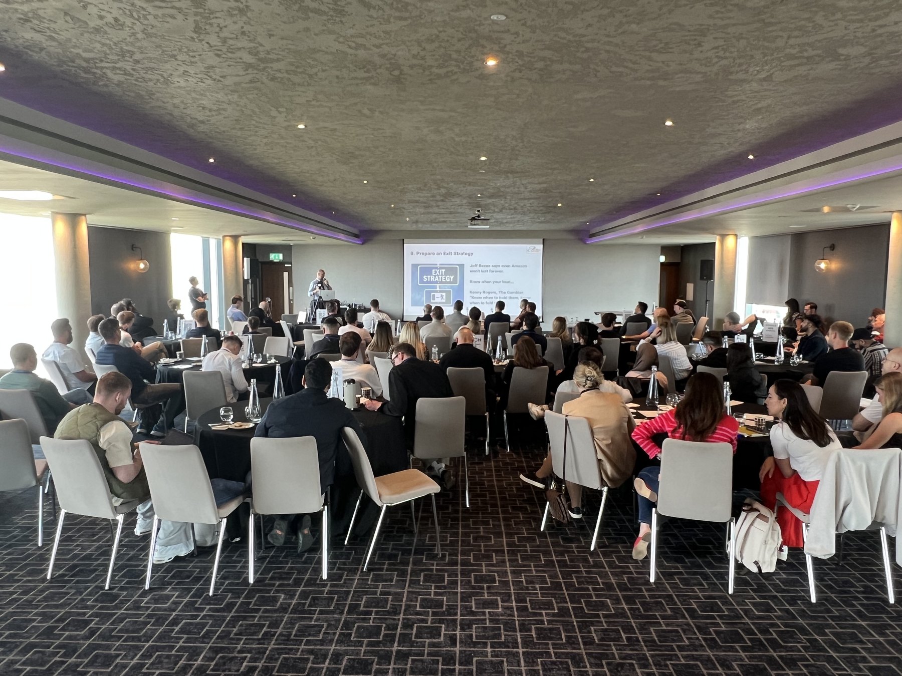 A full conference room at EcommerceCamp in Birmingham, delegates seated at round tables facing a presentation screen