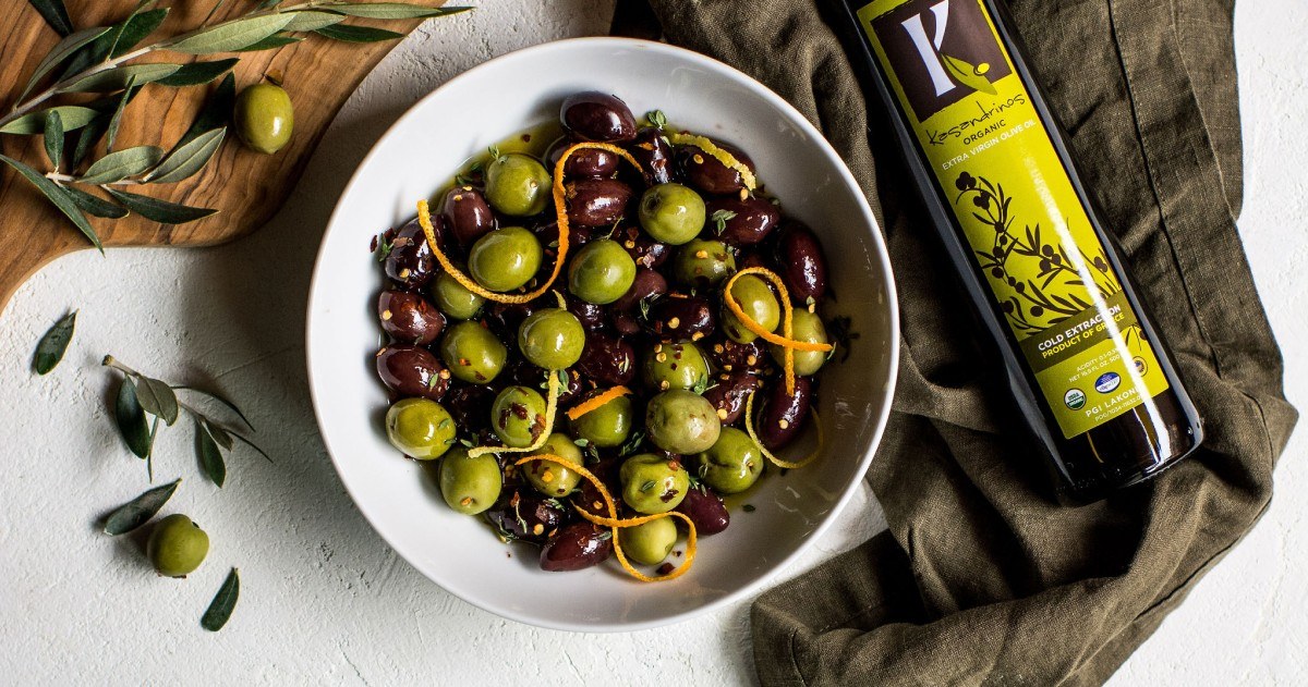 A bowl of marinated olives beside a bottle of Kasandrinos olive oil