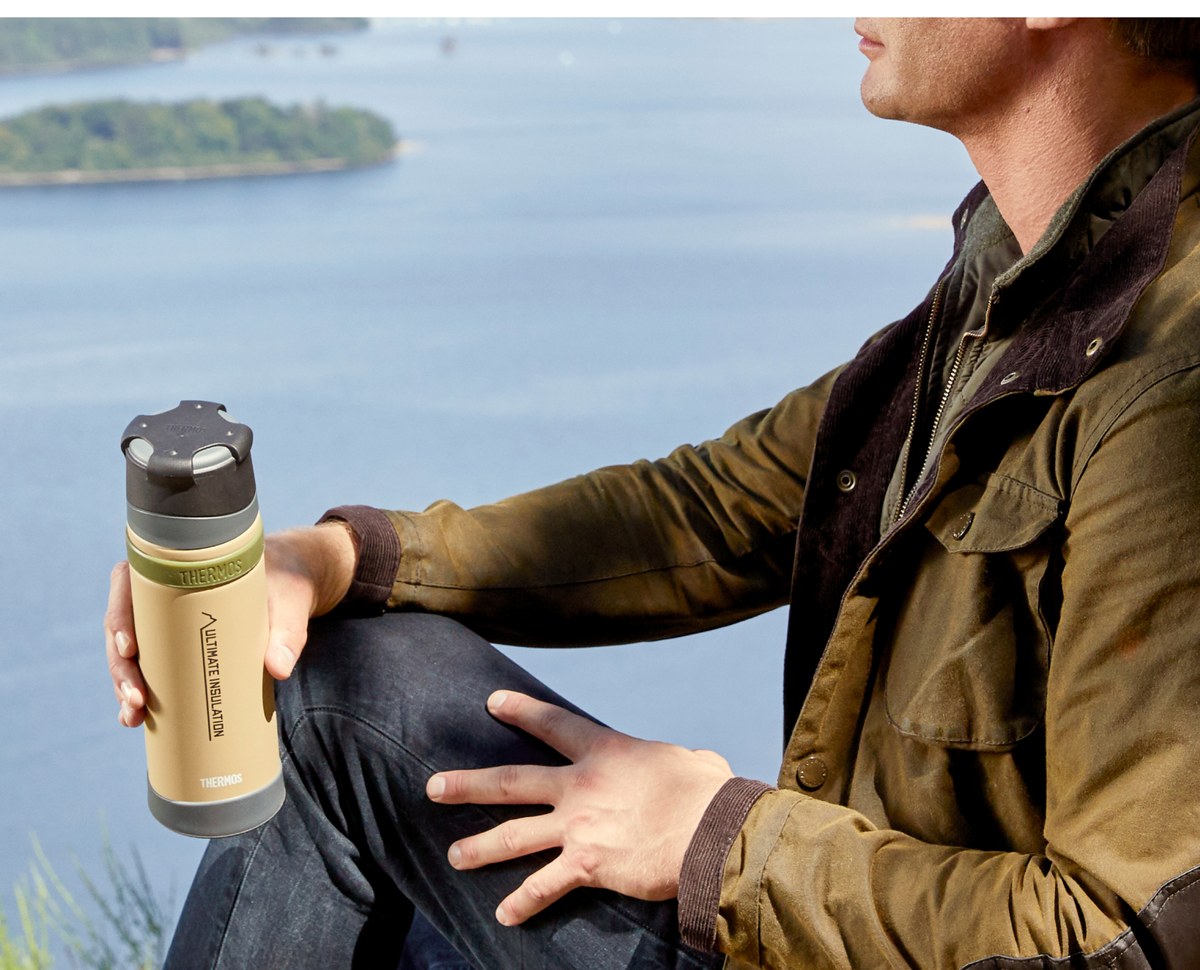 A Thermos flask and food jar on a rock beside a lake