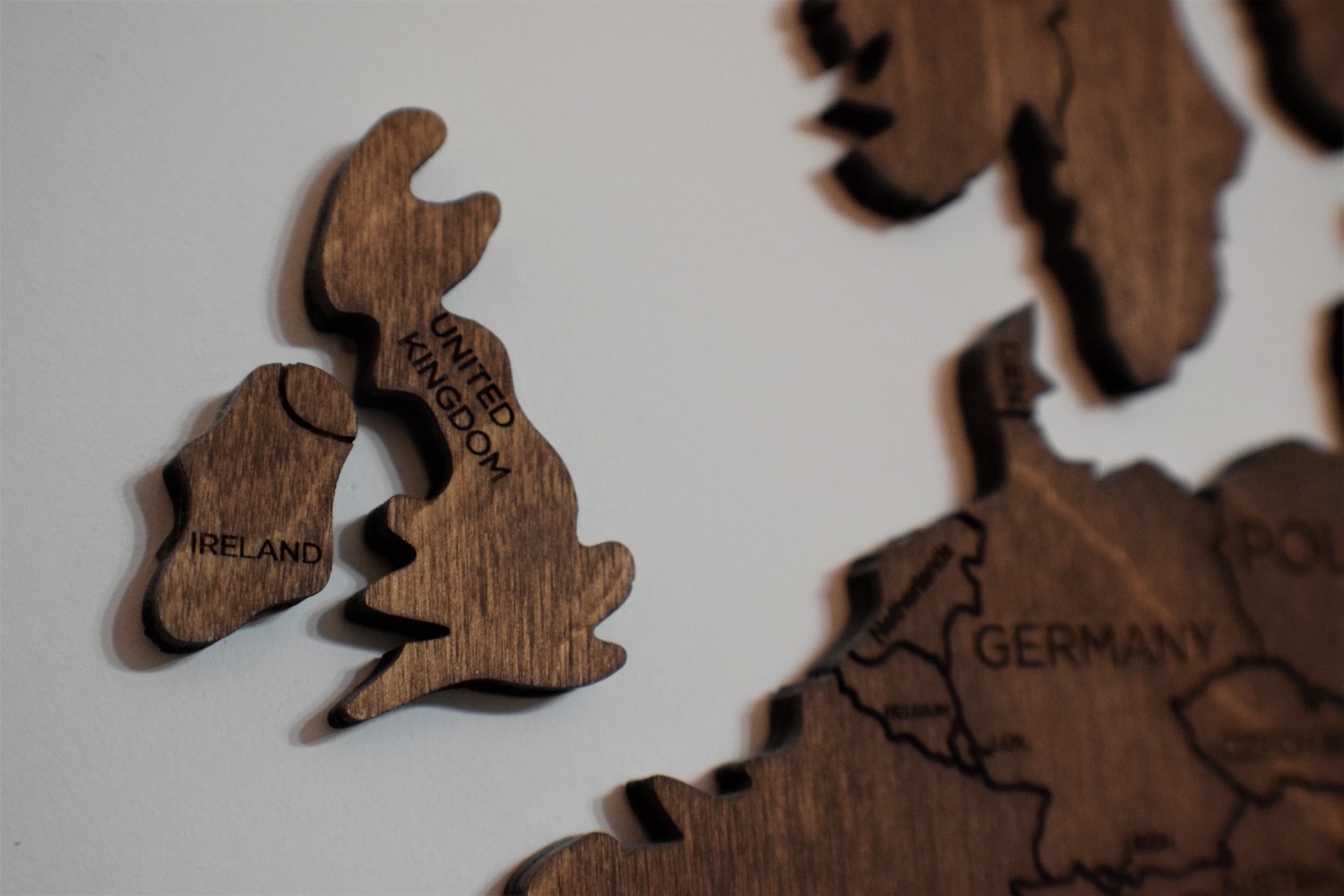 A wooden wall map in close-up, the United Kingdom and Ireland pieces standing slightly proud of the wall with Germany and Poland behind them