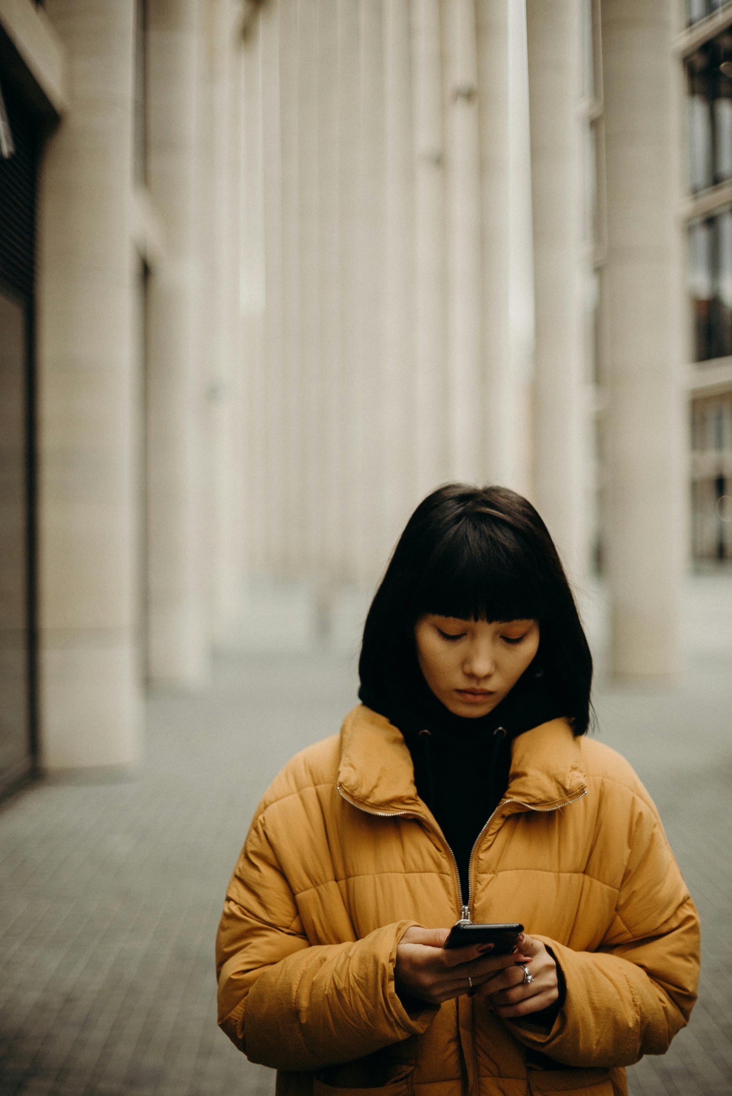 A shopper in a yellow coat searching on her phone in a city street