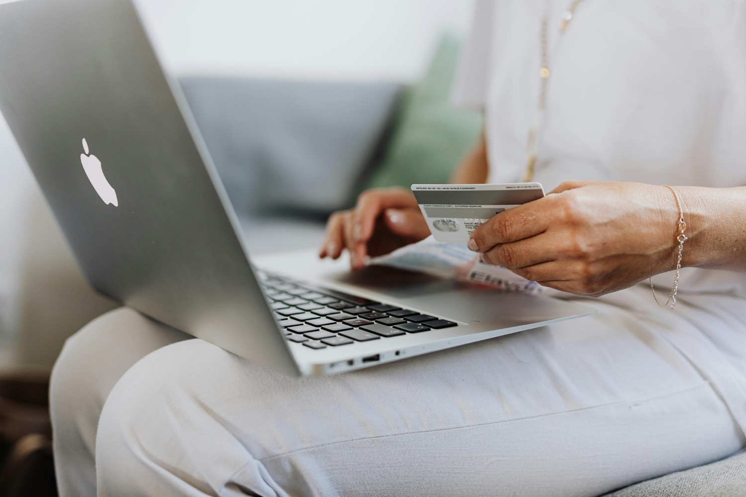 A woman sitting with a laptop on her lap, holding a bank card in one hand while she types with the other