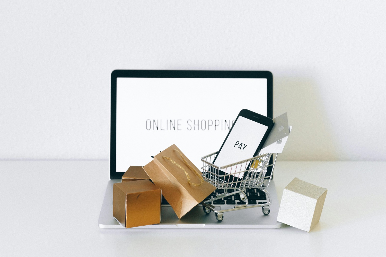 An open laptop with gold gift boxes and a miniature shopping trolley standing in front of it